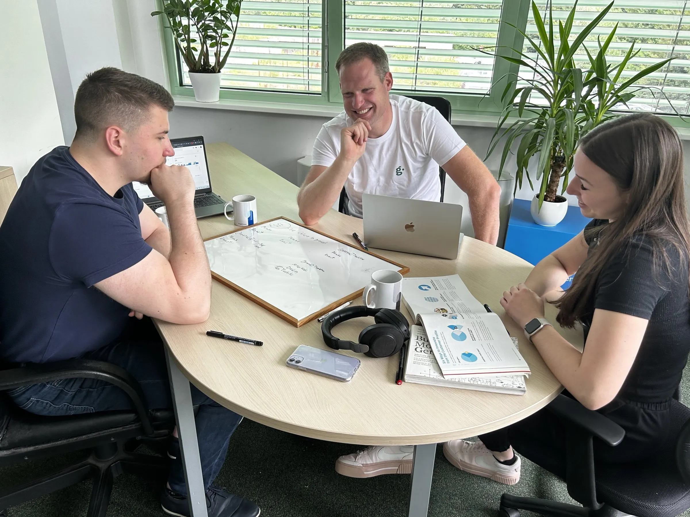 Trije člani ekipe Goodish za okroglo mizo s tablo, prenosniki in škatlo Google Partners ob oknu.